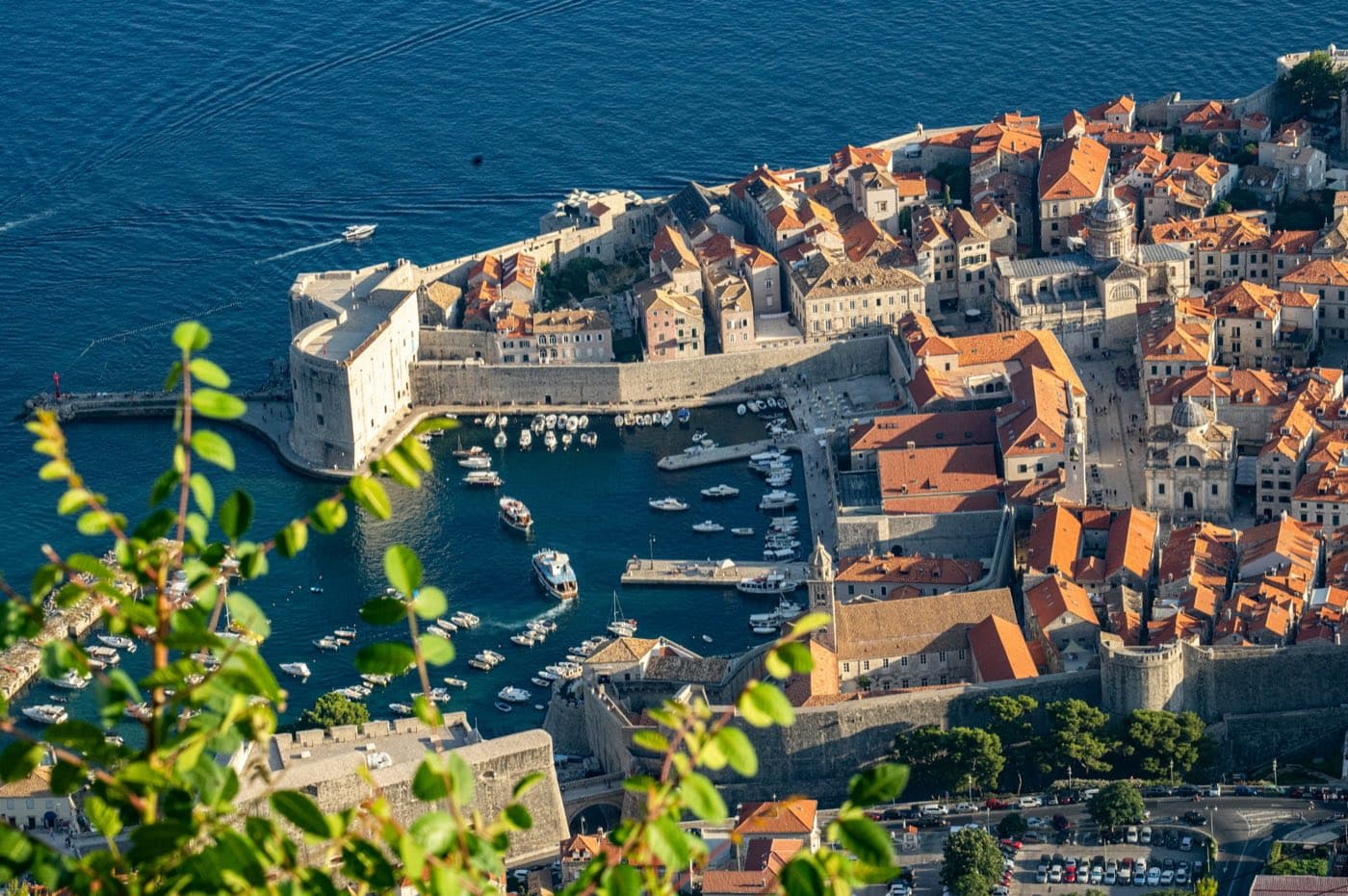 The old town of Dubrovnik with its red tiled roofs and city walls, beside the harbour and the sea.