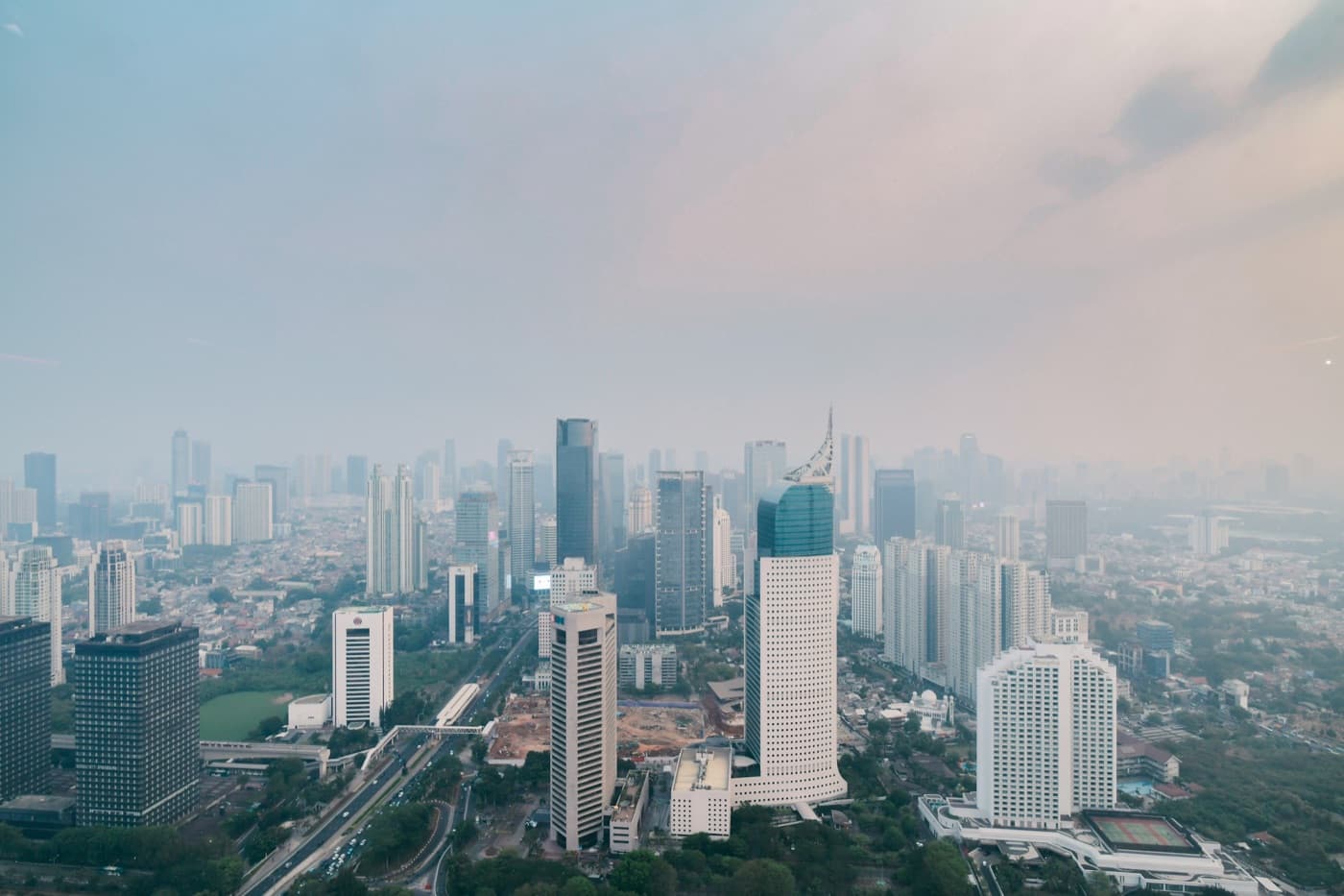 Skyscrapers of Jakarta's central business district rising through haze on a daytime sky.