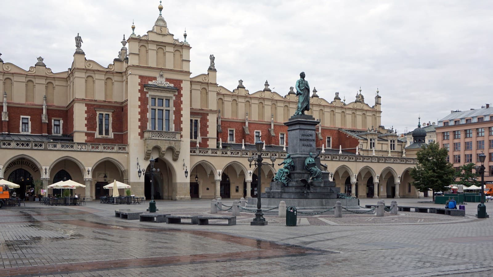 The Cloth Hall on Kraków's Main Market Square under an overcast sky, with the Mickiewicz monument in front of its arcaded red-and-cream facade