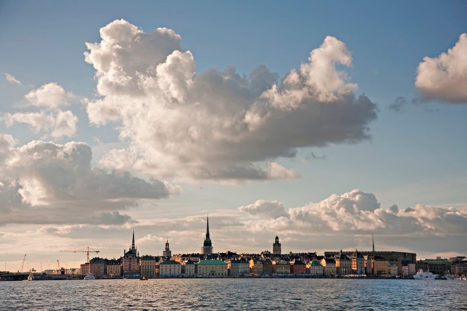 Stockholm's Gamla Stan old town skyline seen across the water at dusk, with spires and waterfront buildings under a cloud-filled sky