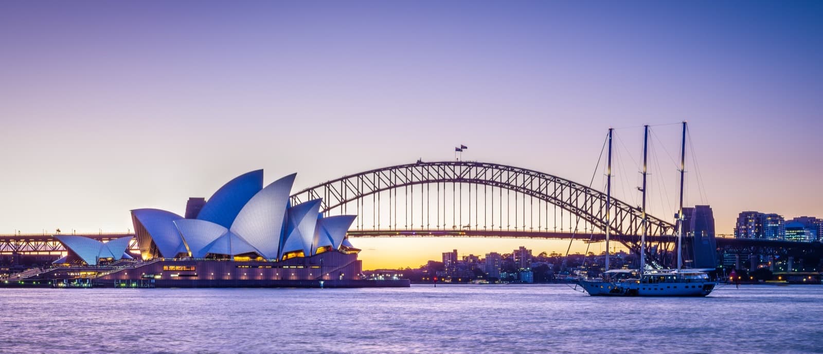The Sydney Opera House and Harbour Bridge at dusk, seen across the harbour